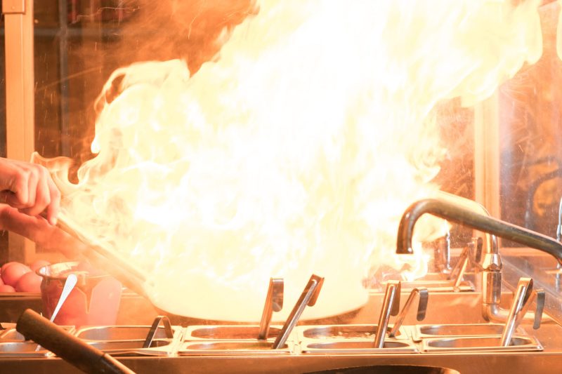 Cook is fry vegetables with spices and sauce in a wok on a flame. Cooking process in an Asian restaurant.